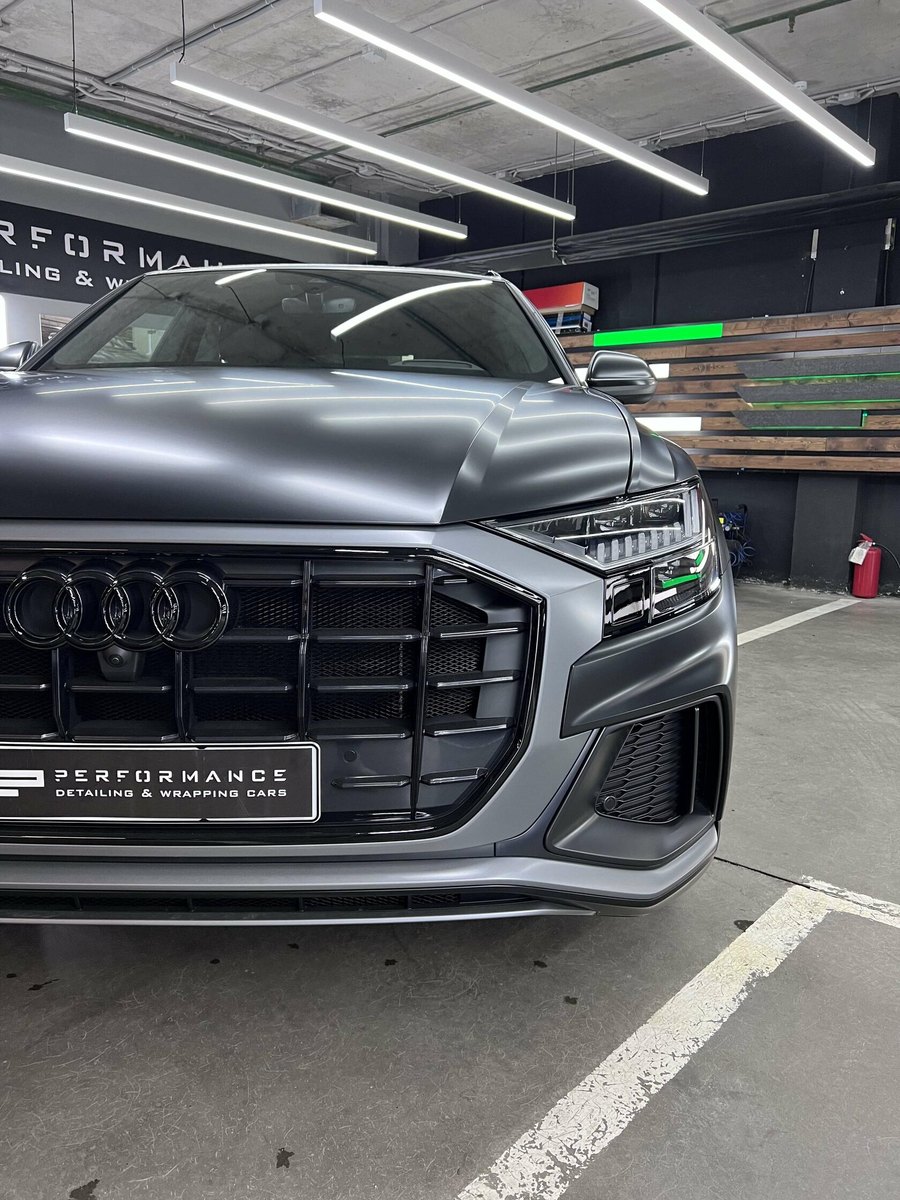 Audi Q8 в серой плёнке у стены с логотипом студии
